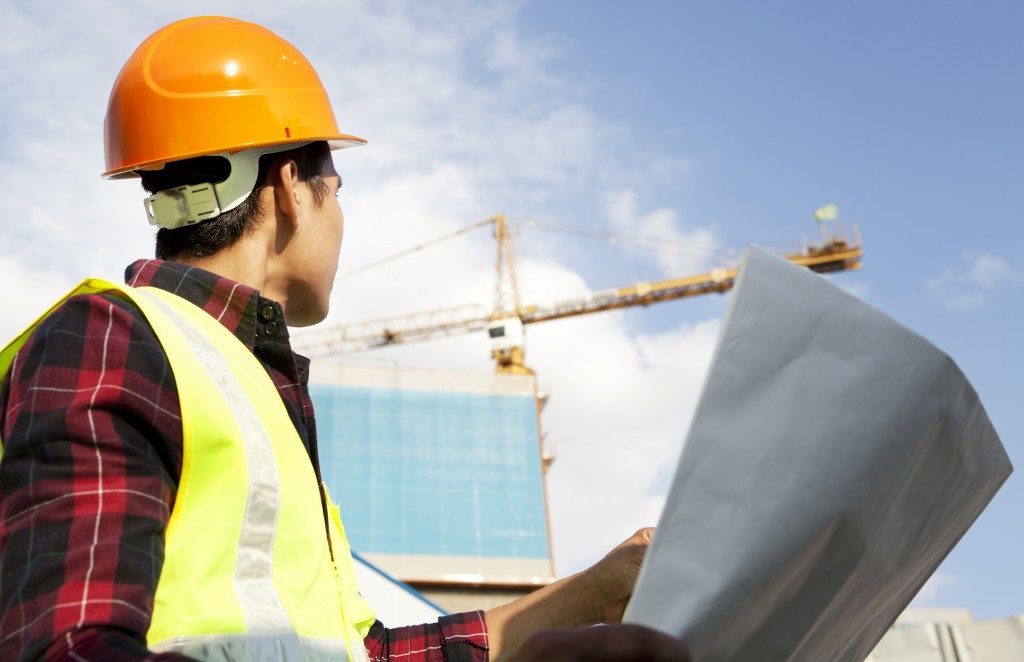 Engineer builder wearing safety vest with blueprint at construction site