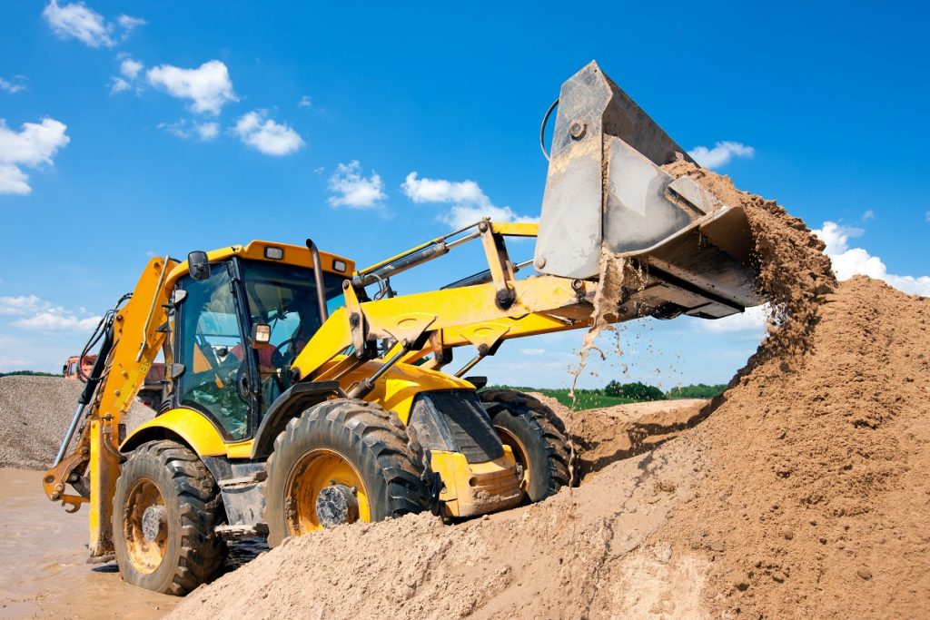 Backhoe loader being used to unload soil by worker