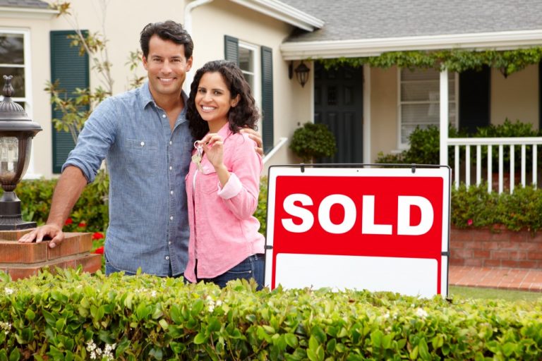 couple outside new home with sold sign