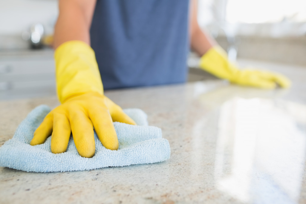 A person wearing yellow rubber gloves wiping the kitchen counter