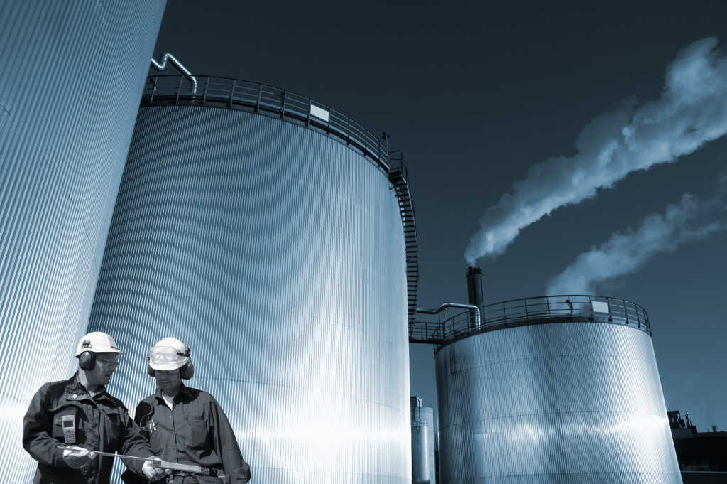 two oil and gas workers, large fuel storage tanks in background, blue toning concept